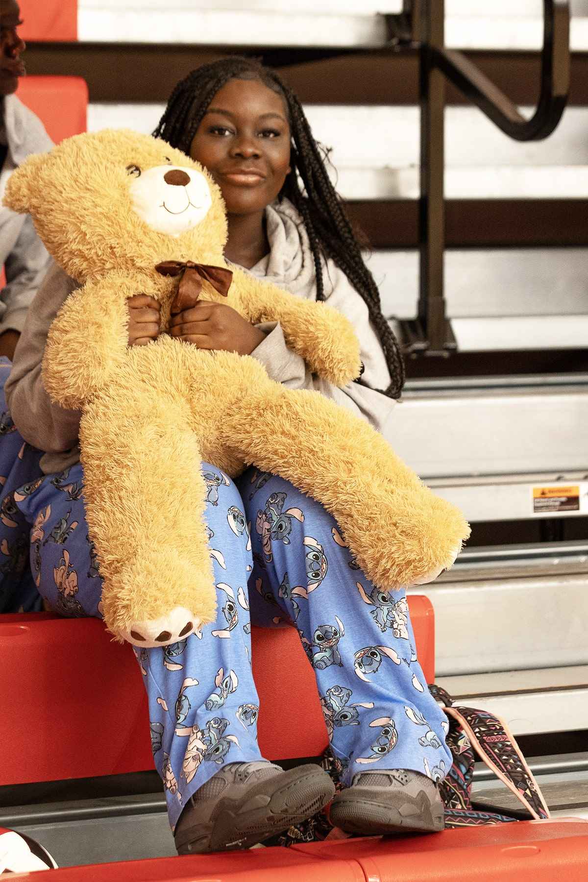 A girl sitting on a bench, gently holding a teddy bear in her lap, with a serene expression on her face.