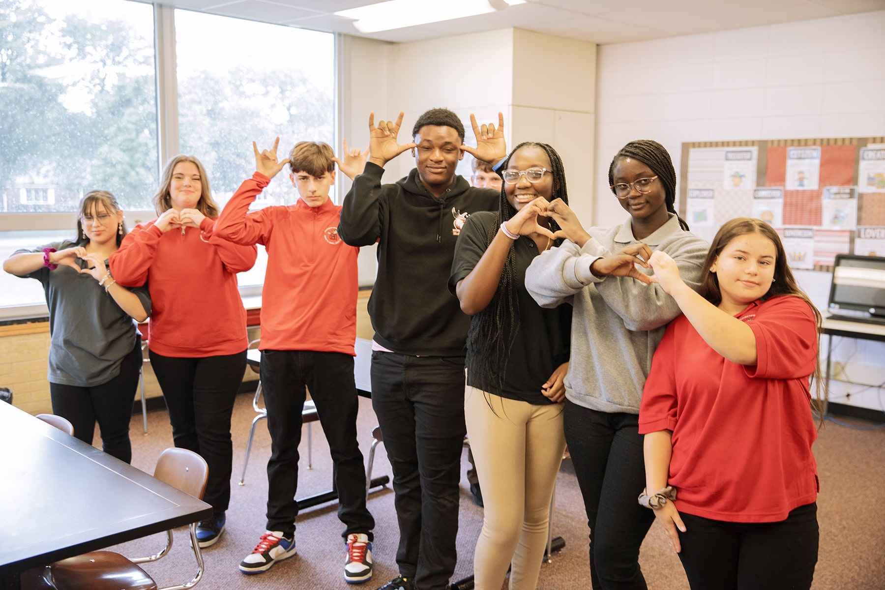 A group of students wearing red shirts stands together in a classroom, engaged in conversation and learning.